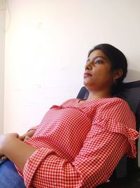 Young woman looking away while sitting on wall at home