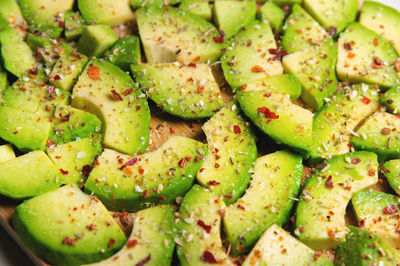 Large slices of sliced ripe avocado lie textured on a wooden cutting board. sprinkled with spices