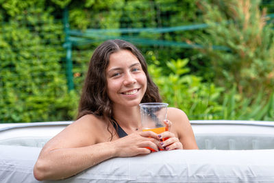 Gorgeous teenage girl with long, dark hair and glass with drink in the garden inflatable pool
