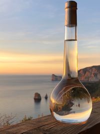 Close-up of glass on table against sea during sunset