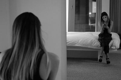 Young woman reflecting on mirror while using mobile phone in bedroom