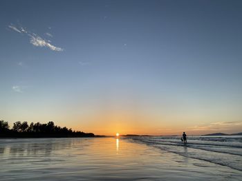 Silhouette person by lake against sky during sunset
