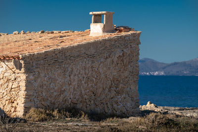 Old building by sea against clear blue sky