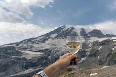 Cropped image of man hand holding wineglass against snowcapped mountain