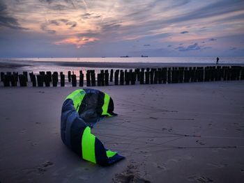 Wooden posts by parachute on beach against sky during sunset