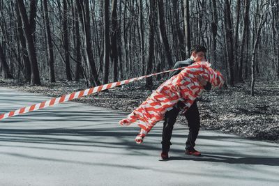 Man carrying friend wrapped in cordon tape on road