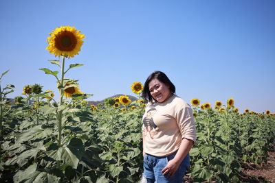 Portrait of beautiful woman standing by sunflower field against clear sky