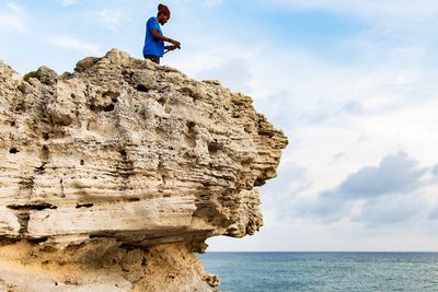 People on rock by sea against sky