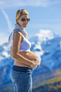 Portrait of smiling pregnant woman standing against mountains