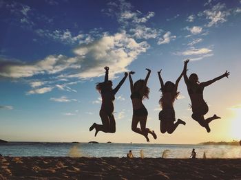 Silhouette female friends jumping on sand at beach