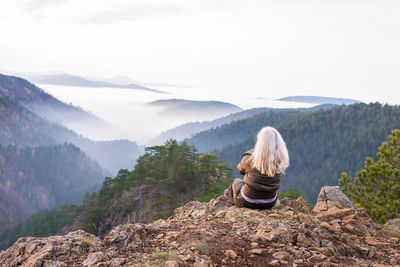 Woman hiker on a mountain top looking to low clouds and hills breaking through