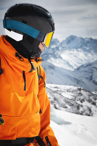 A professional skier athlete in a red jacket, helmet and mask stands on a slope against the backdrop