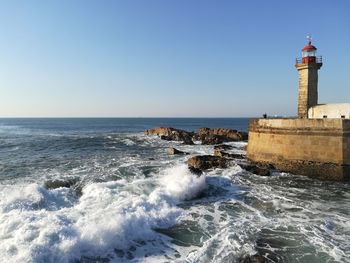 Lighthouse by sea against clear blue sky