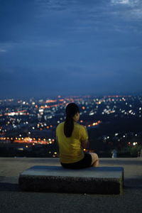 Woman sitting on illuminated cityscape against sky at night