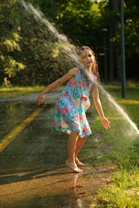 Happy six year old girl playing with a water sprinkler in the summer sunlit park