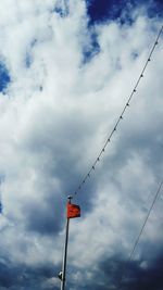 Low angle view of birds perching on power line against cloudy sky