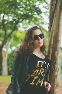 Portrait of teenage girl sunglasses standing by tree trunk