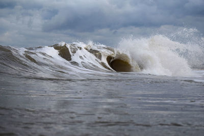 Waves splashing on shore against sky