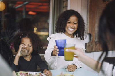 Cheerful girl toasting drinks with woman while having dinner at restaurant