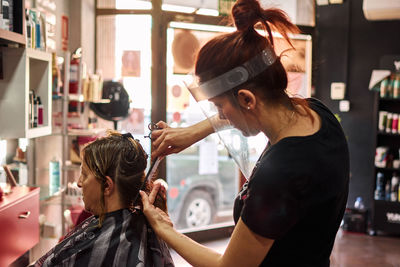 Hairdresser cuts a client's hair with a face shield