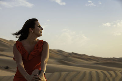 Woman looking away while sitting on land against sky