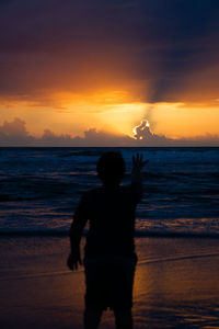 Silhouette man standing on beach against sky during sunset