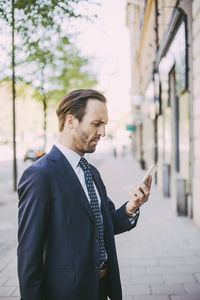 Side view of businessman using phone in city