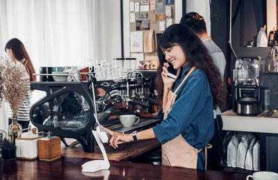 Smiling barista talking on mobile phone in cafe