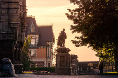 Statue in city against sky at sunset