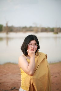 Portrait of young woman standing against lake