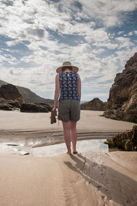 Full length rear view of woman standing at beach against sky