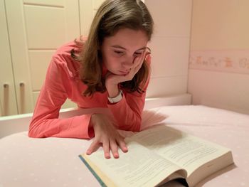 Girl reading book on bed at home