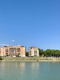 Buildings by trees against clear blue sky