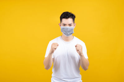 Portrait of young man standing against yellow background