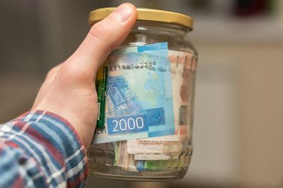 Cropped hand holding jar with paper currencies