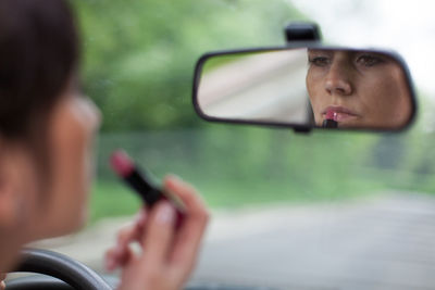 Reflection of woman applying lipstick on rear-view mirror in car