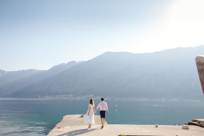 Rear view of couple walking on pier against clear sky