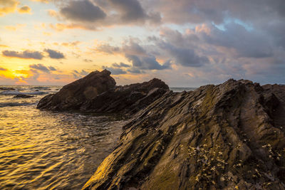 Rock formations by sea against cloudy sky during sunset