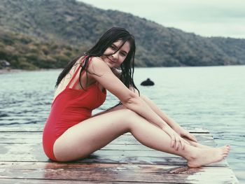 Side view full length portrait of sensuous woman relaxing by sea on pier