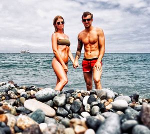 Portrait of couple holding hands while standing on rock at beach