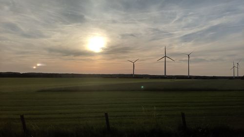 Wind turbines on field against sky during sunset