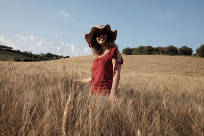 Full length portrait of smiling young woman standing on field against sky