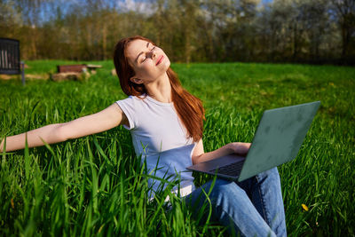 Young woman using laptop while sitting on field