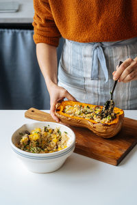 Crop housewife filling baked butternut pumpkin with vegetarian mix of quinoa and vegetables at white table in home kitchen