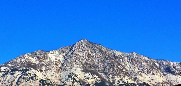 Low angle view of snowcapped mountains against clear blue sky