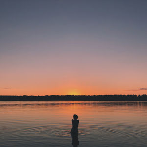 Silhouette woman standing in lake during sunset