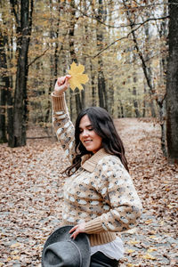 Side view of a smiling young woman standing by tree