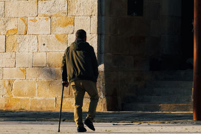 Rear view of man walking on footpath against wall