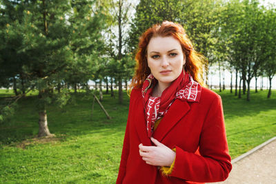 Portrait of a cute woman in a red coat against the background of a green park