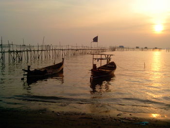 Boats moored in sea against sky during sunset